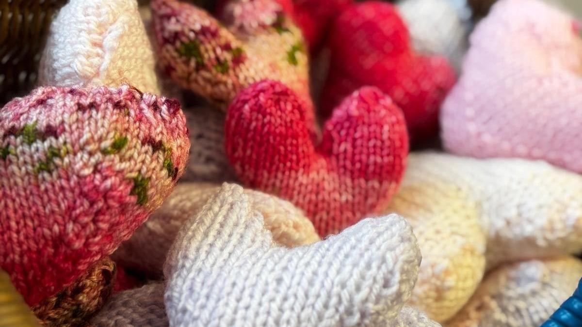 A close-up of colourful knitted hearts - they are dark pink, light pink, green and white.