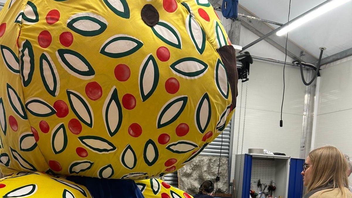 A close up of a large toy rabbit's head towering over a visitor who has come to look at it. The toy is yellow with white petals on the material and red spots. It has a black nose and eyes.