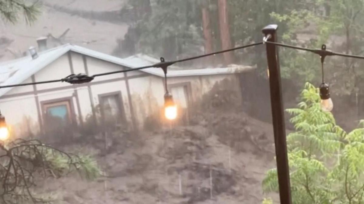 A house is swept along a brown river of raging flood water.