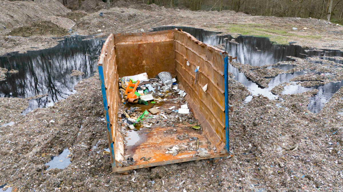 Waste container with some rubbish inside sitting on cleared land