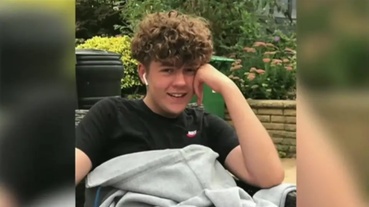 Olly Stephens, a boy with dark curly hair and wearing a black -shirt. He's resting his head on one hand and smiling at the camera.