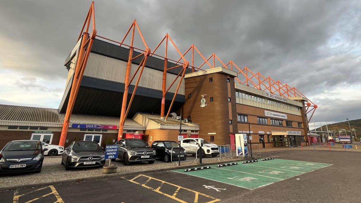 ICT stadium and its car park. There are dark clouds above the football ground.