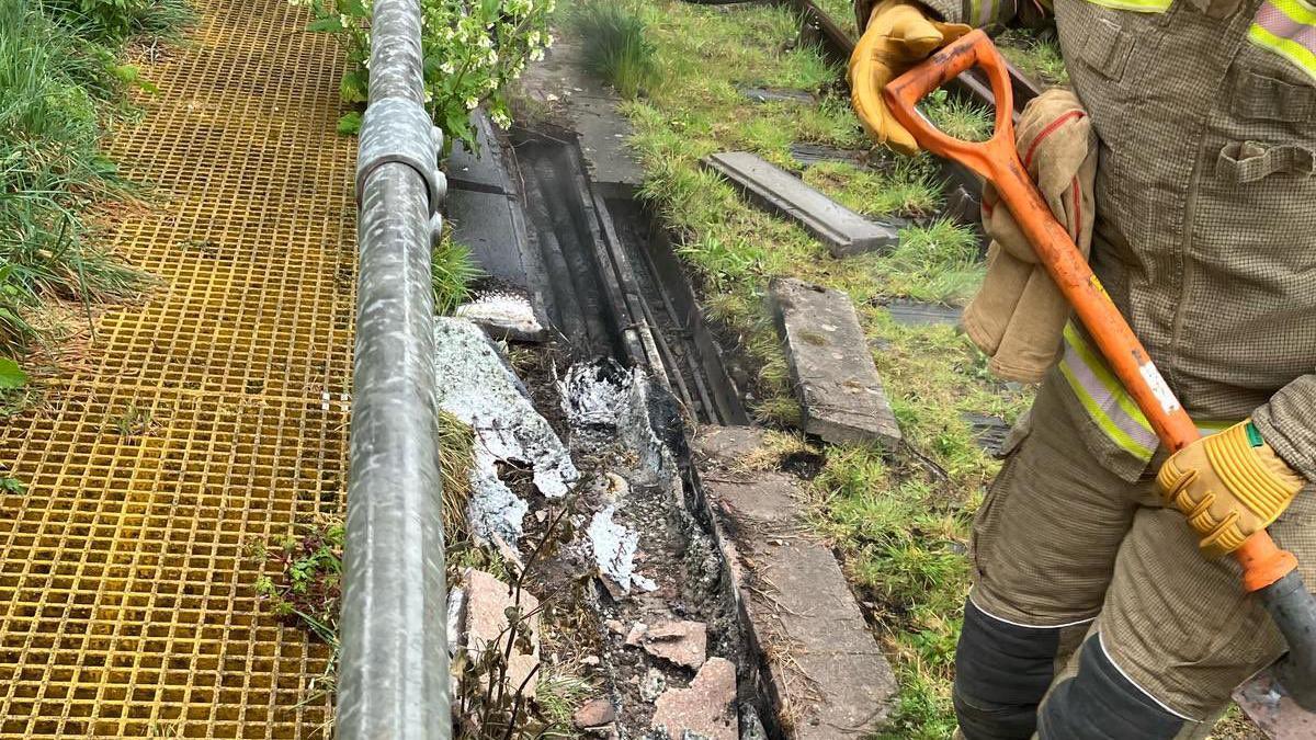 A man in holding a shovel is inspecting a train track that is damaged by fire.