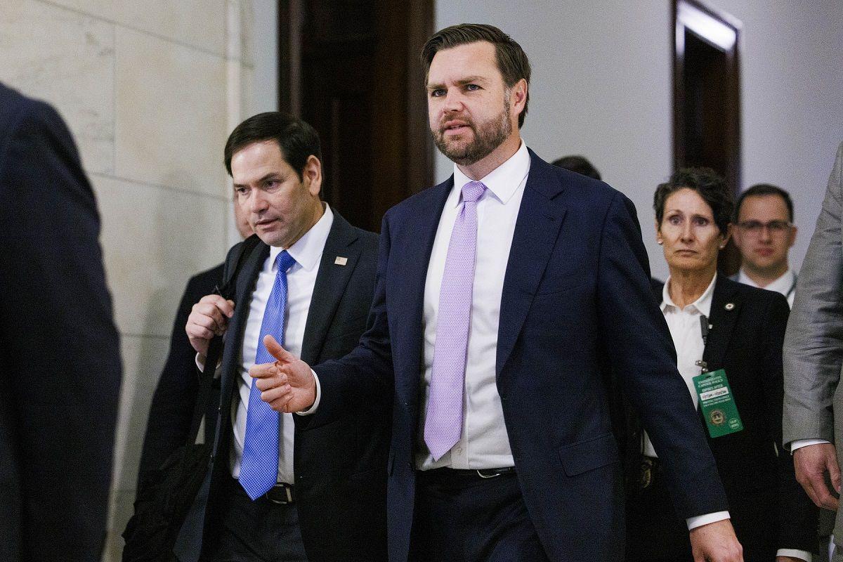 Rubio trailing behind Vance, both men wearing suits in an office setting