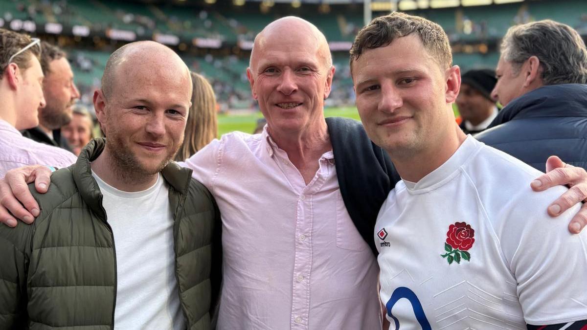 Fraser Dingwall is standing pitch side at Twickenham in his white England shirt, next to his brother Euan and father Gordon. 