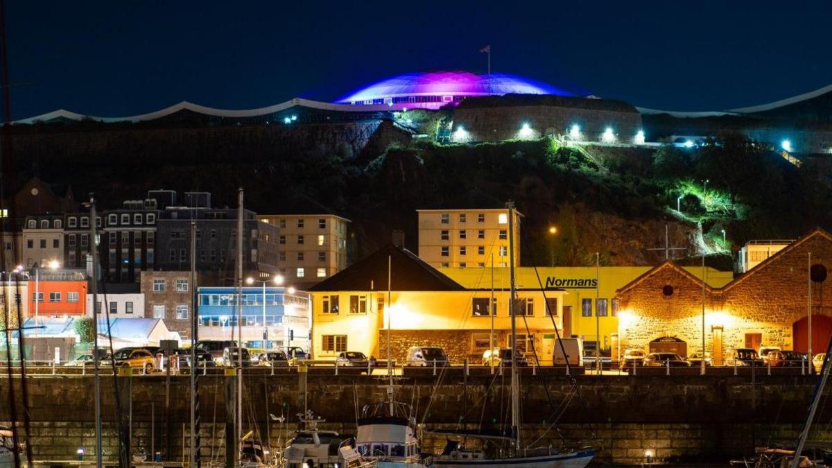 Fort Regent's dome in Jersey is lit up blue and pink.