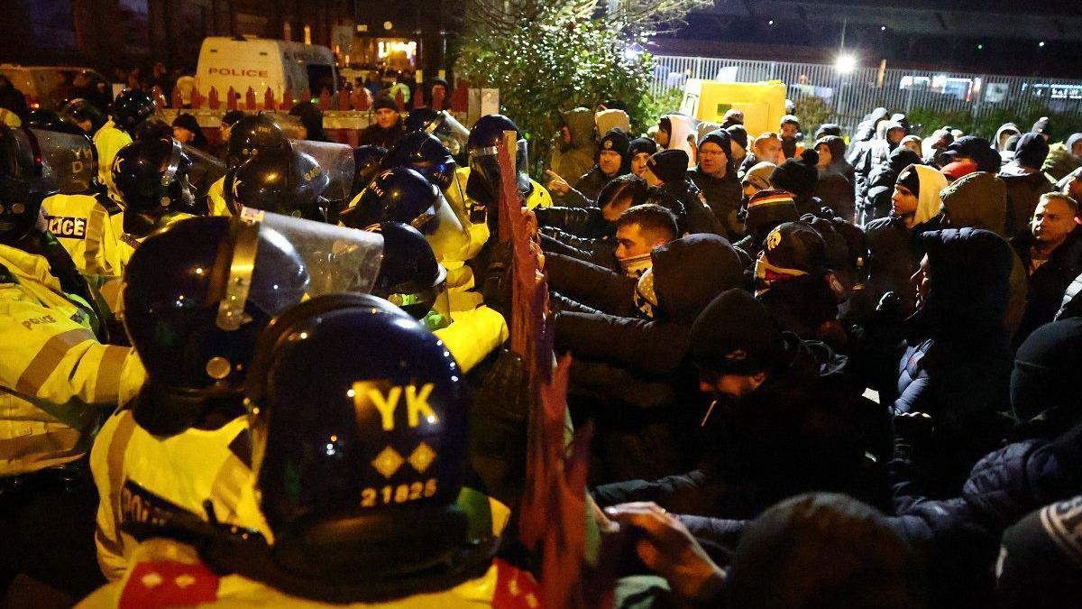 Fans and police officers clash outside the stadium before the match. Police officers are standing on one side of a barrier and the fans are pushing against it.