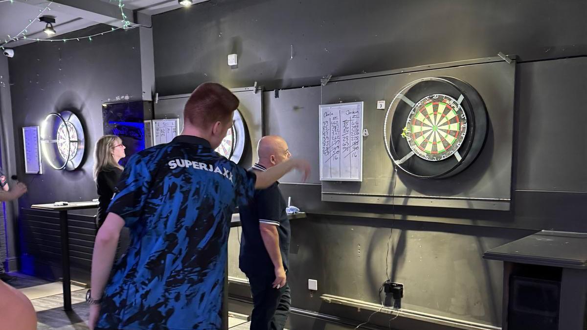 Jackson throwing a darts at a board while wearing t-shirt saying "Super Jaxx"