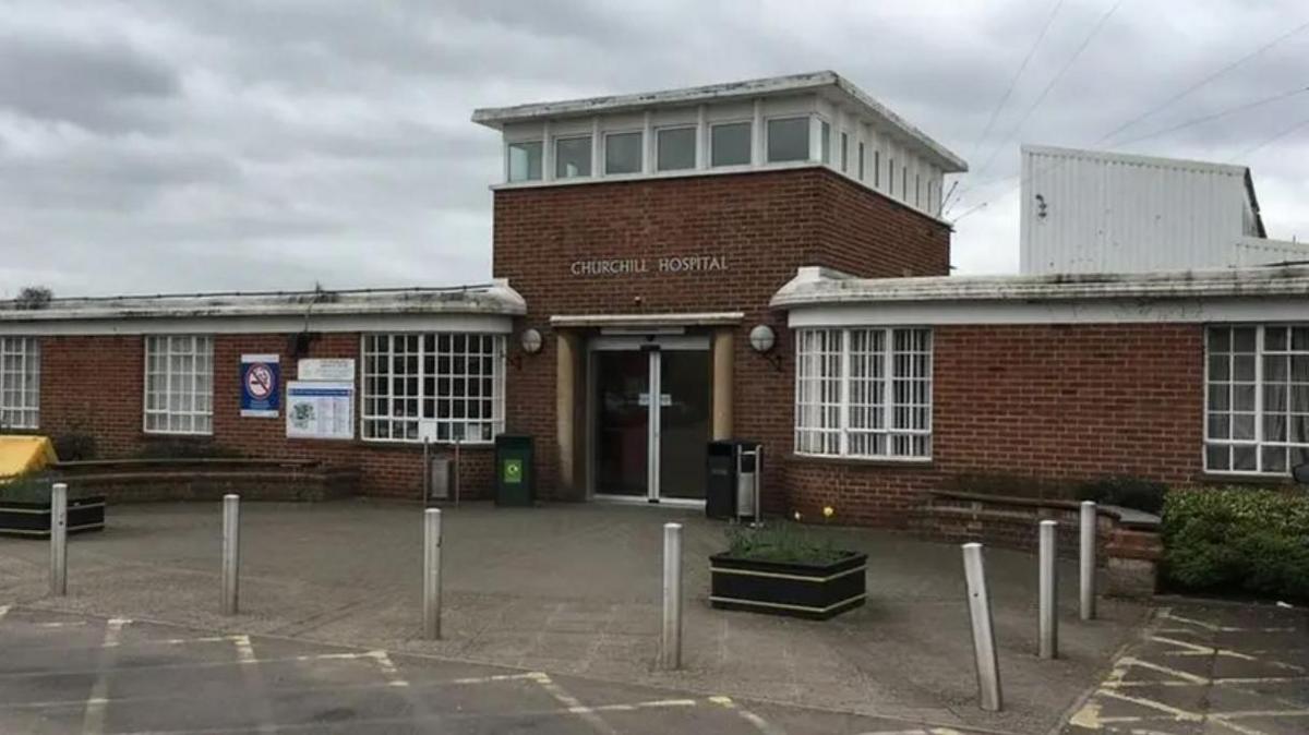 Outside the Churchill Hospital in Oxford on a cloudy day. The car park in front of the building is empty.