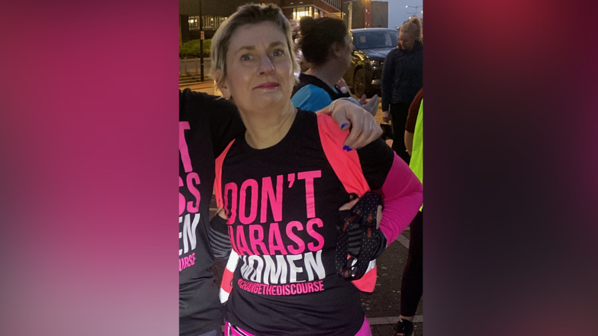 Llun yn dangos dynes mewn siorts pinc llachar, mewn crys-t due a phinc yn darllen 'Don't Harass Women' arno.