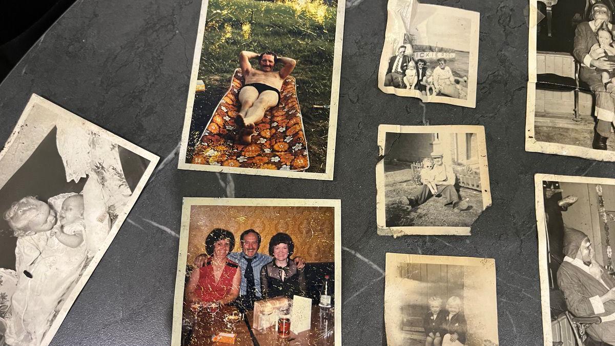 Family photos are spread out across a kitchen table, showing black and white images of children and families as well as a few colour images.