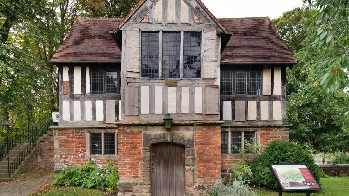 Kings Norton Old Grammar School is a brick and timber-built two-storey building, with a large wooden entrance door, in its own grounds, with a set of stone steps on the left.