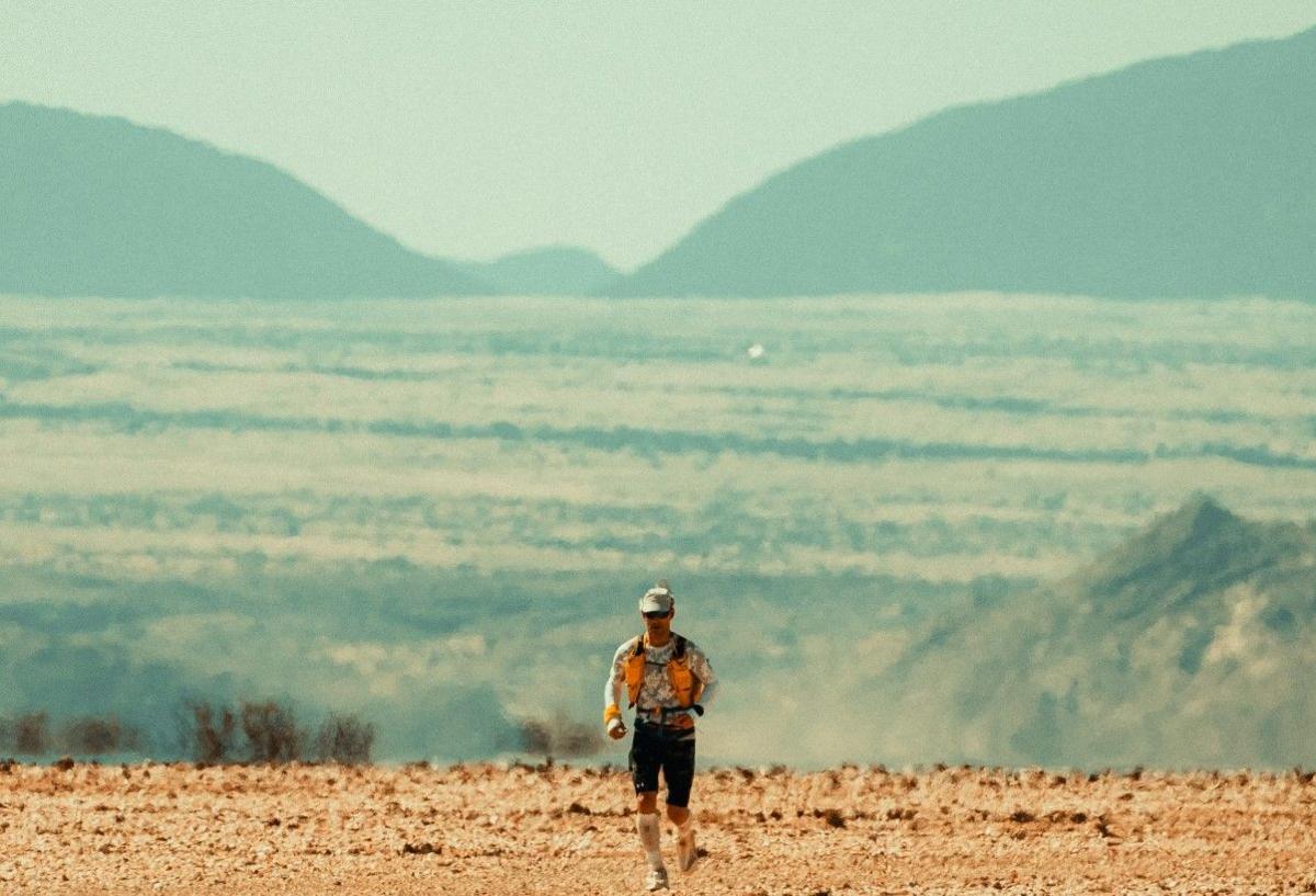 Jon Shield is seen from head to toe running - a small part of the image near the bottom in the centre. A mountain landscape is in the distance. 