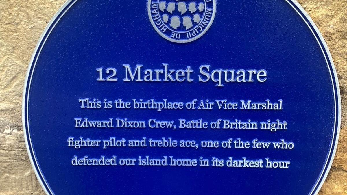 A close-up of wording of the blue plaque. It reads: 12 Market Square. This is the birthplace of Air Vice Marshal Edward Dixon Crew, Battle of Britain night fighter pilot and treble ace, one of the few who defended our island home in its darkest hour.