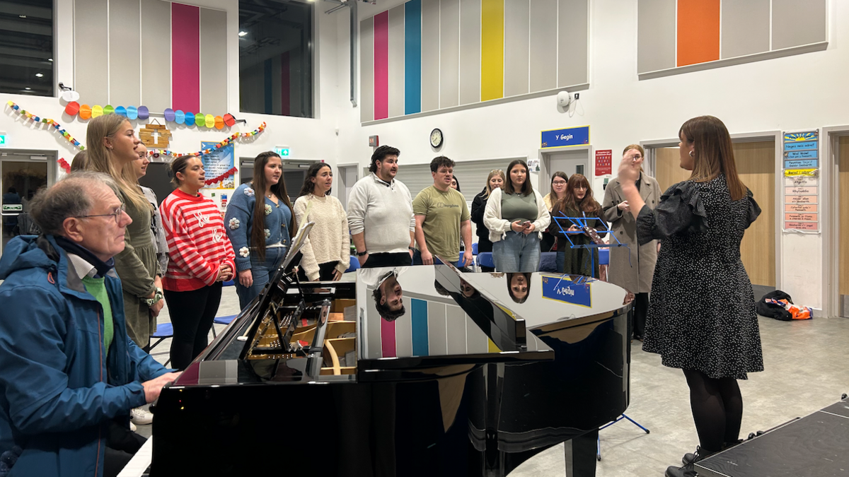 Côr Dur a Môr yn ymarfer mewn neuadd ysgol gynradd. 