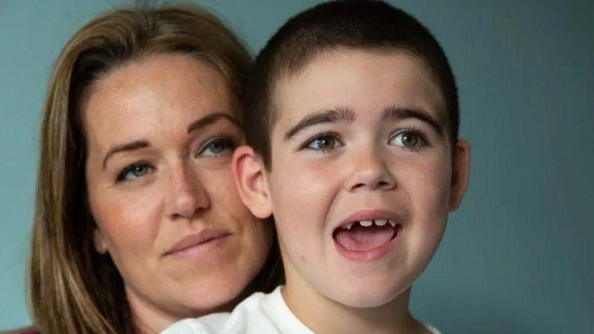 A woman on the left with brown hair behind a boy with his mouth open. A light blue background is behind them.