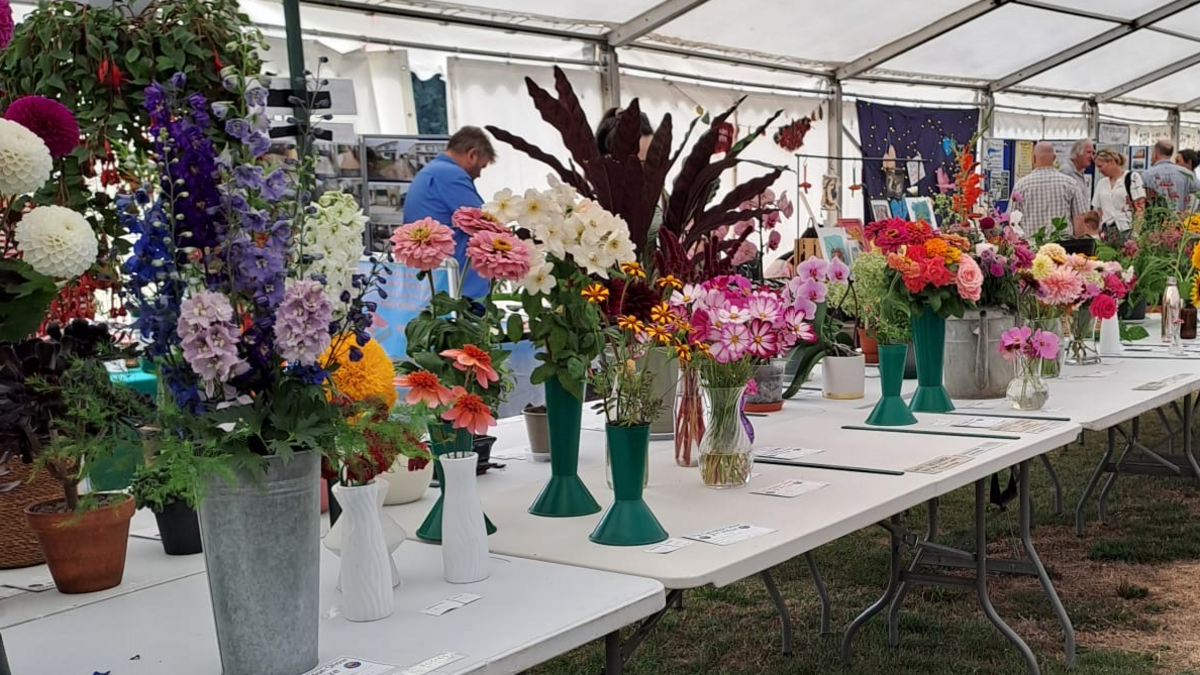Trestle tables in a marquee, filled with colourful flowers in vases. a few people behind the tables