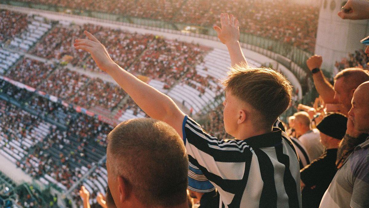 Newcastle fans, in their black and white striped shirts, in the stadium cheering. 