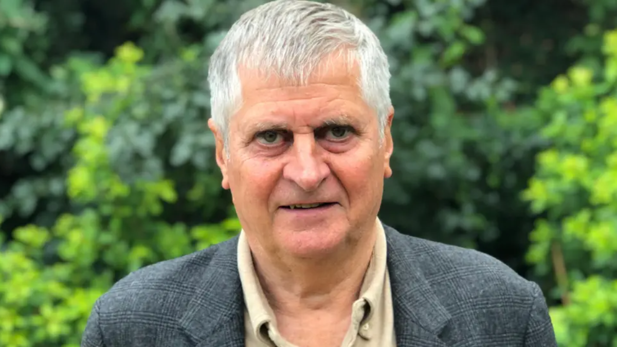 A close up of Rob Prow looking into the camera. He has short grey hair, is wearing a grey jacket and light shirt. He is standing in front of some greenery.