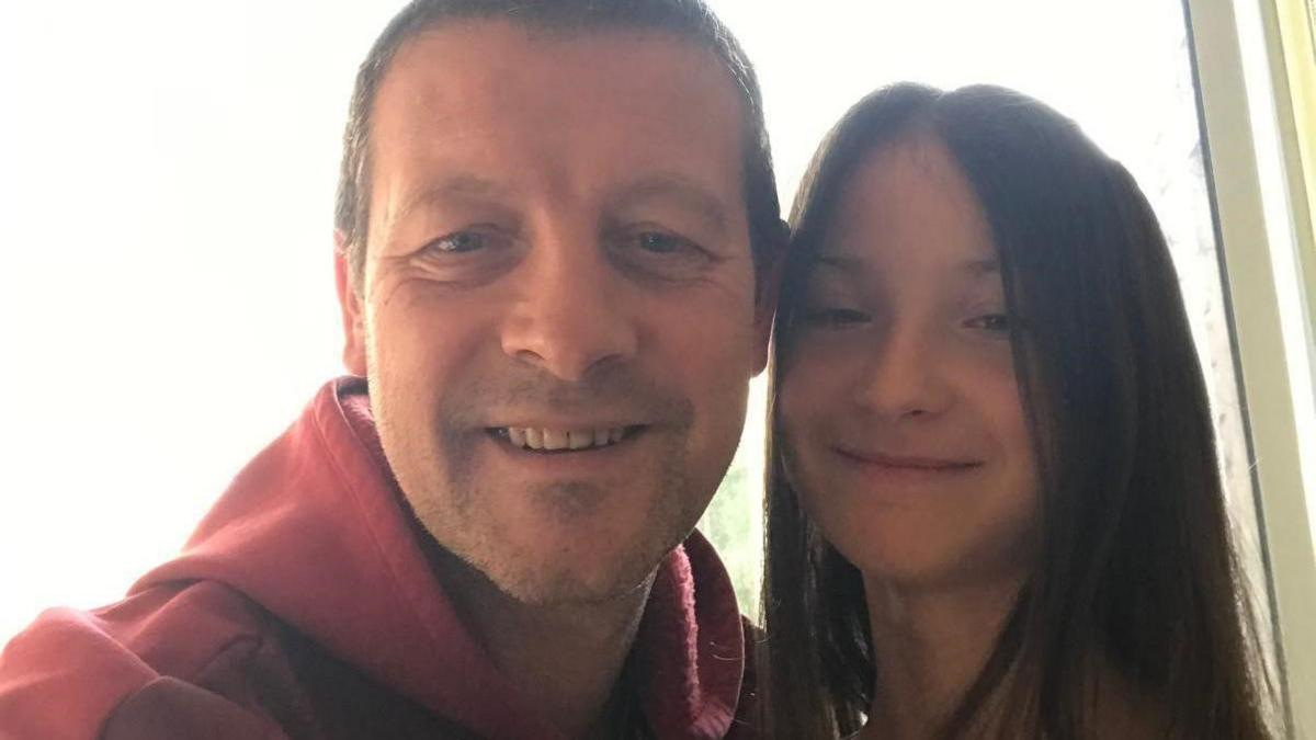 A father and daughter pose for a selfie. The background is overexposed but they are both smiling in the image. 