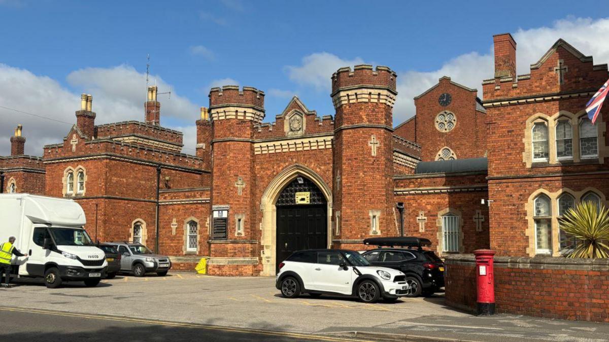 The entrance to Lincoln prison, with a large black door and two turrets with five cars parked at the front