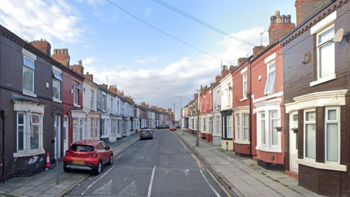 A road of terraced houses with three cars parked in the street