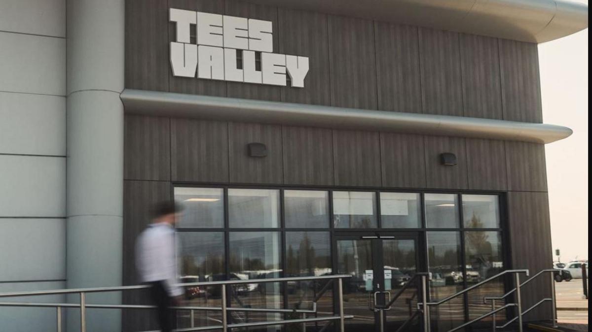 Part of the front of a building with glass panels around a glass front door. There are metal rails leading to the front door with the blurred figure of a man walking towards it. A sign at the top of the building reads "Tees Valley".