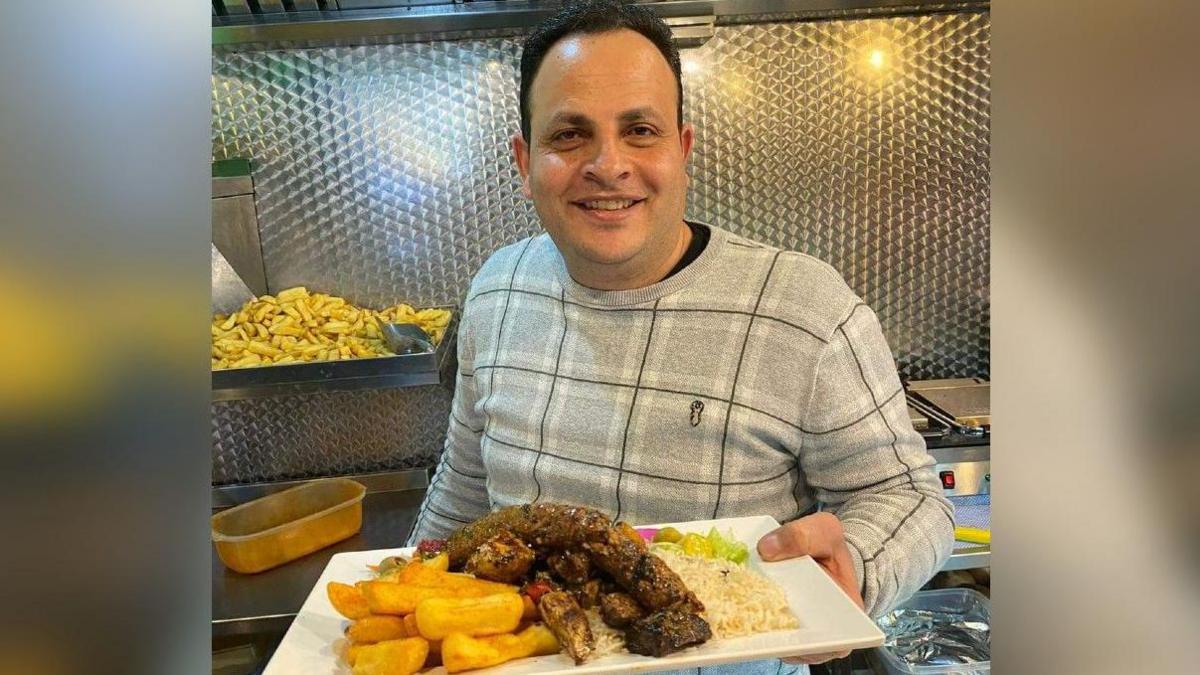 Owner Wael Garas smiling and holding a plate of chips, meat, rice and salad from restaurant Middle Feast.