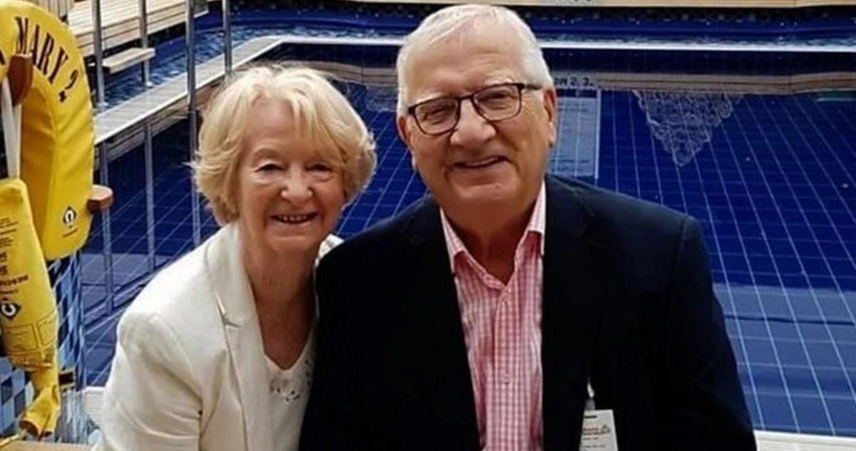 Ian Marsh-Rees, in a black suit with a gingham shirt, with wife Valerie, who is in a white jacket. They are smiling stood in front of a swimming pool