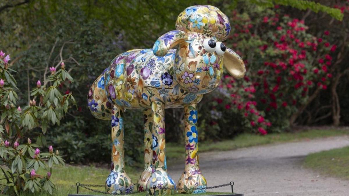 A model of animated character Shaun the Sheep is painted in pastel shades. The sculpture is covered with flowers and fruit