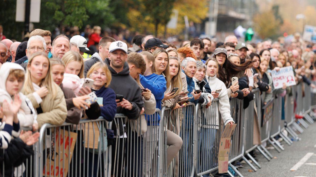 A line of hundreds of spectators watching from behind the metal railings on the route.