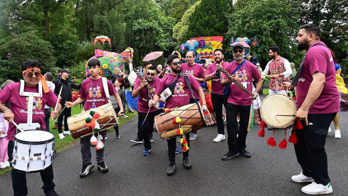 A group of men wearing purple t-shirts are wearing drums which they are playing as part of the events at the Belfast Mela in 2023