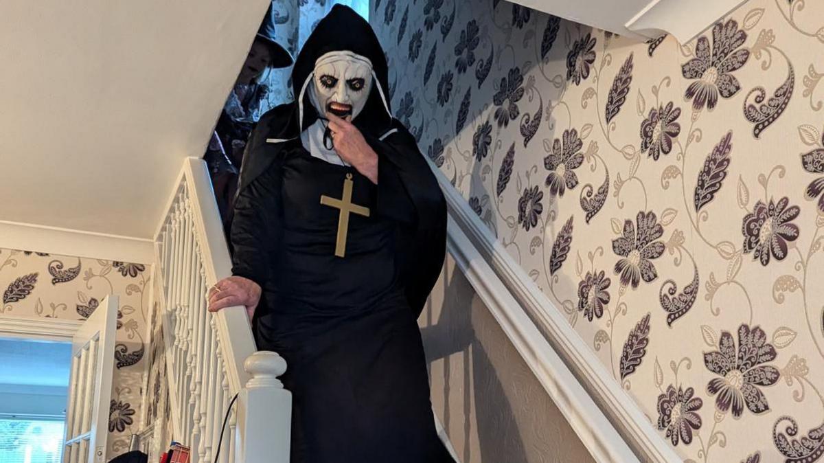 Ms Fisher's mother Ingrid in her spooky nun costume walking down stairs inside the house