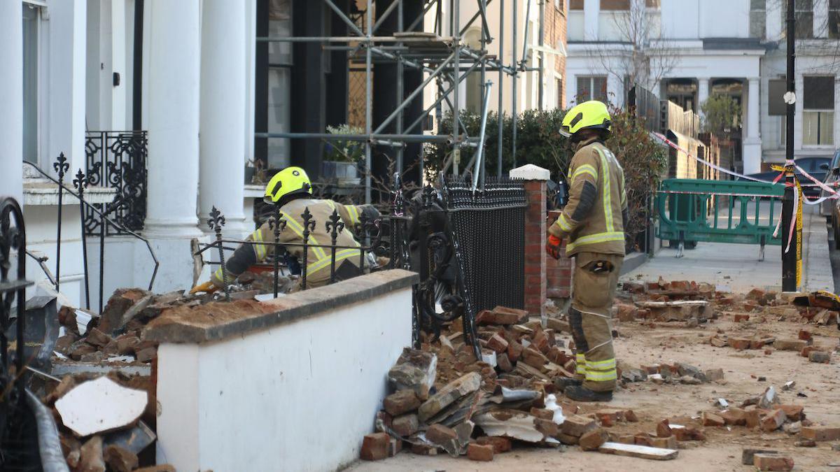 Two firefighters look towards a property that has suffered a partial collapse.