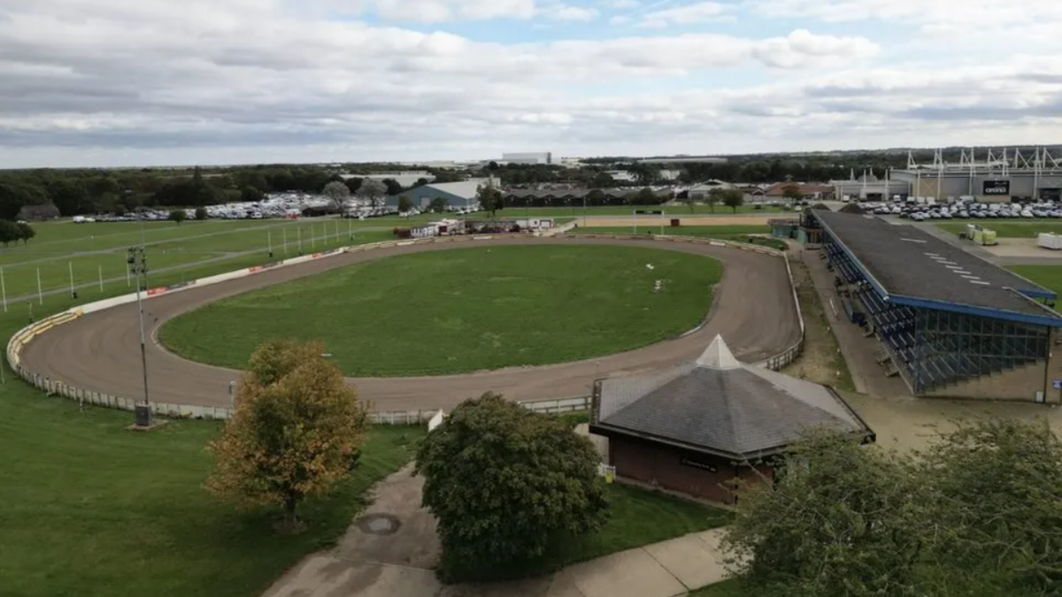 Aerial view of the speedway track on the showground, with spectator stand to the right and buildings in the distance. 