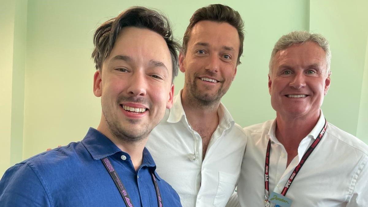 Alex Jacques wears an indigo blue shirt. He is standing to the left of the picture. In the centre is Jolyon Palmer. On the right is David Coulthard. Both are wearing white shirts. Jacques and Coulthard both have lanyards round their necks. All three are looking at the camera and smiling.