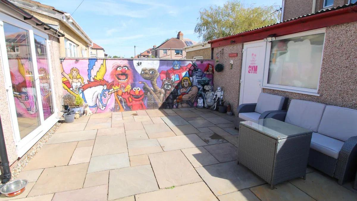 A garden patio with a wall featuring paintings of '80s pop culture characters.