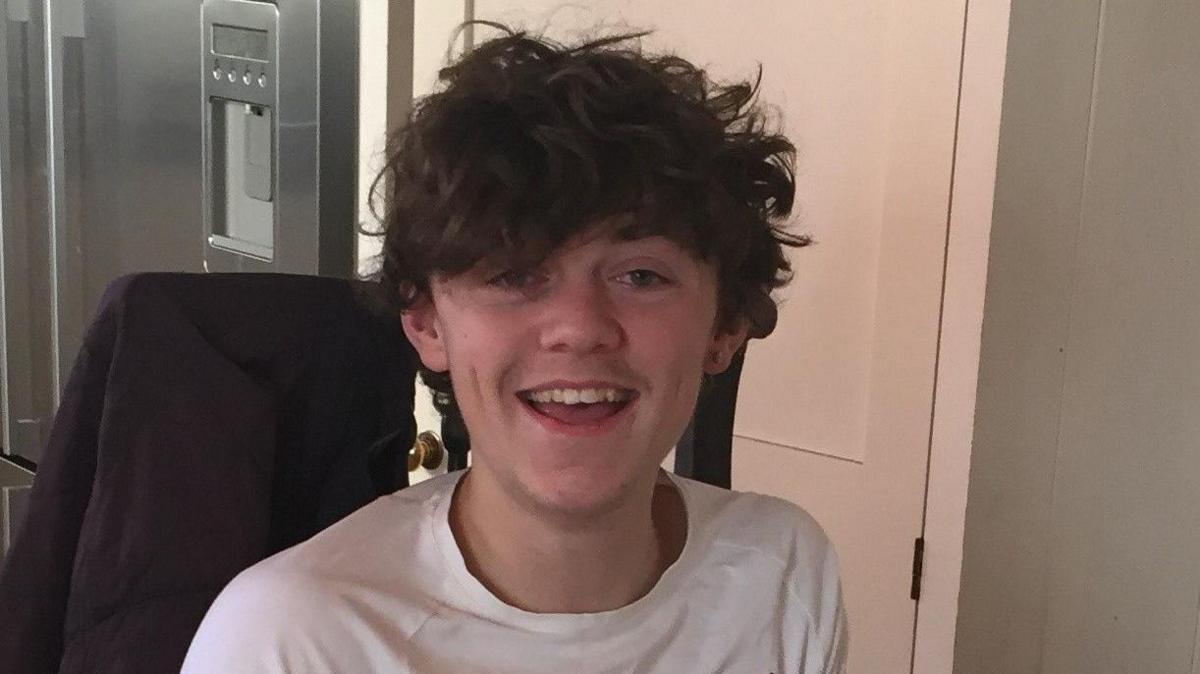 Harry Coopland, a young man with brown hair, is smiling and wearing a white T-shirt.