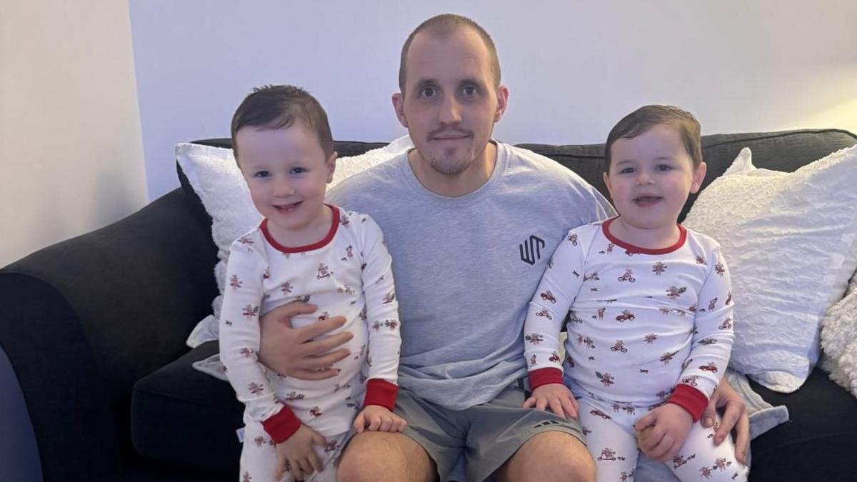 Keenan yn eistedd ar soffa gyda'i feibion, yn eu dillad nos, naill ochr iddo