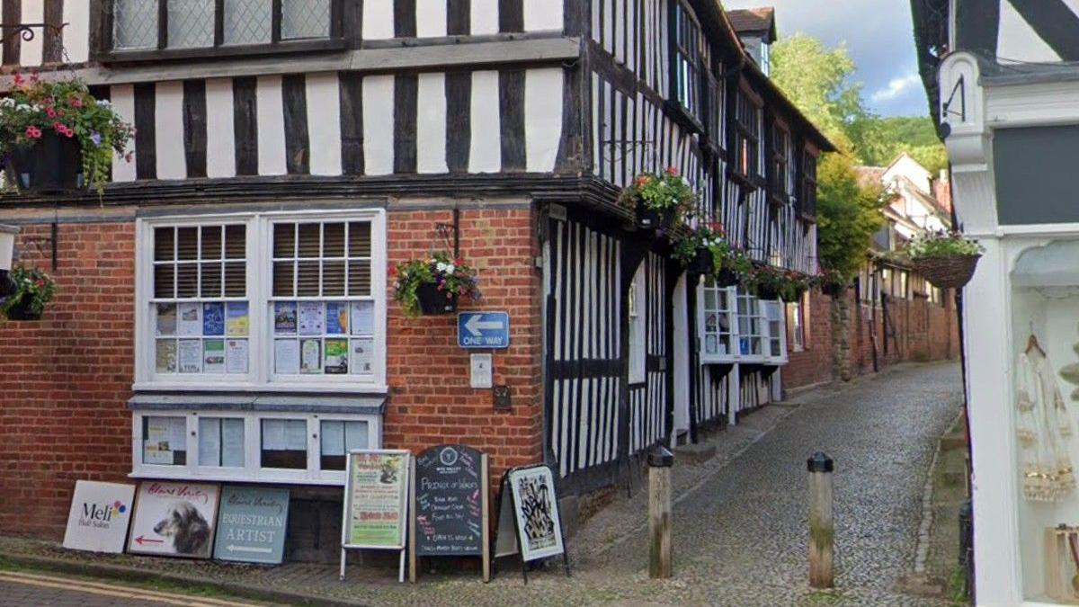 A historic street in Ledbury. There are signs for boutique shops and a narrow alleyway. 