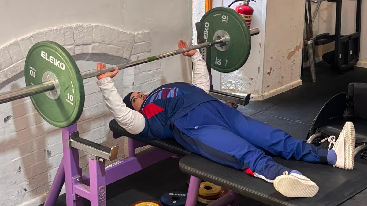 Doaa Shayea trains in the gym in Plymouth. She is laying down, lifting a weight with both hands while wearing a tracksuit