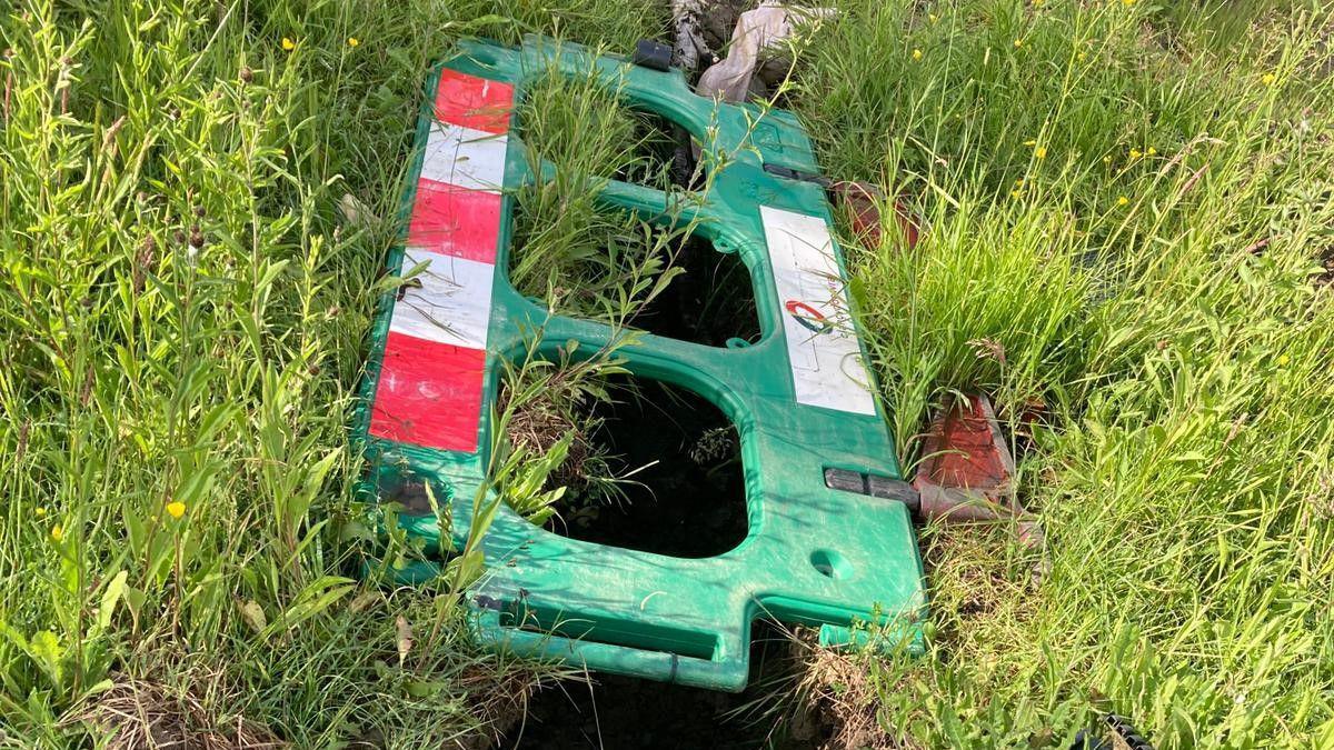 A trench in some grassland, about one foot wide and several feet long, has been covered by a green piece of fencing but there are holes in it which would be easy to fall through