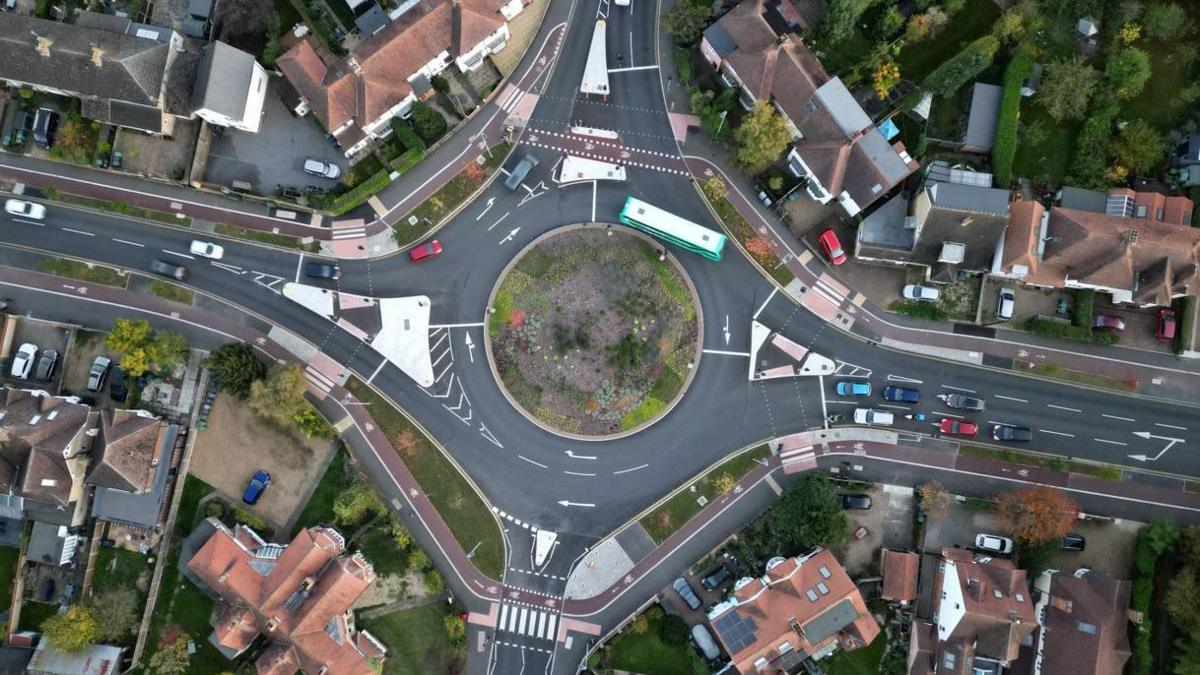 Aerial view of a roundabout. A red cycle lane is visible on roads to the left and right and on the roundabout itself.