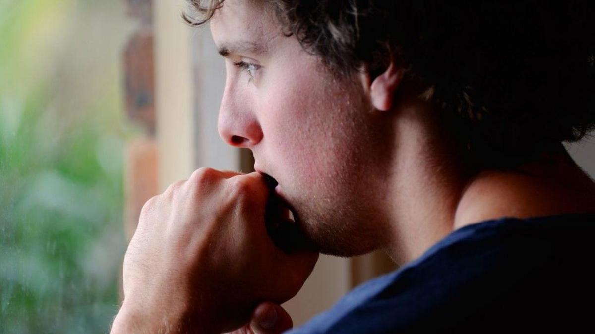 A young man looking worried staring out of a window