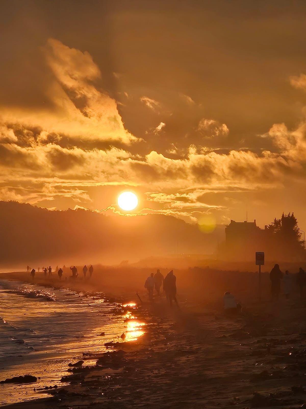 An orange sunset sky over Broughty Ferry beach with people silhouetted along the shore.