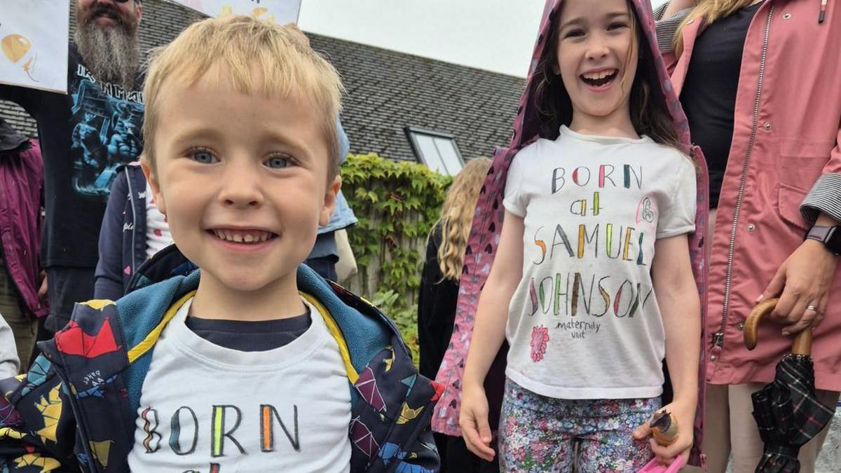 Two children, a boy and a girl, smiling at the camera with t shirts that say "born at Samuel Johnson"