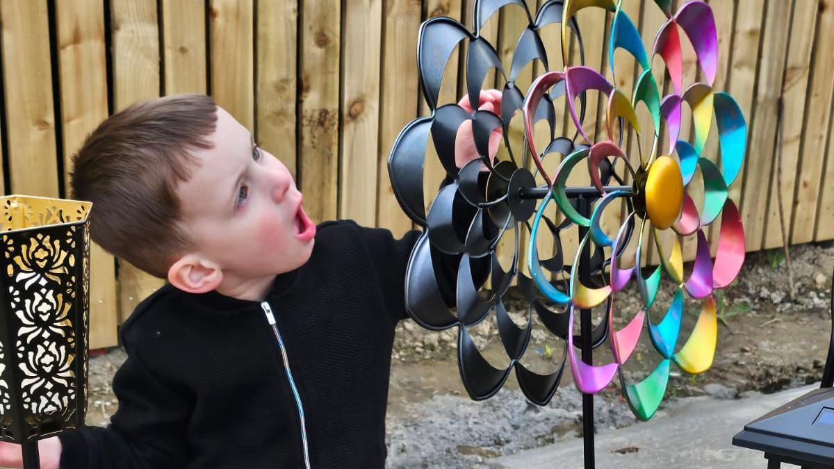 A boy wearing a black jumper looks at a colourful windmill