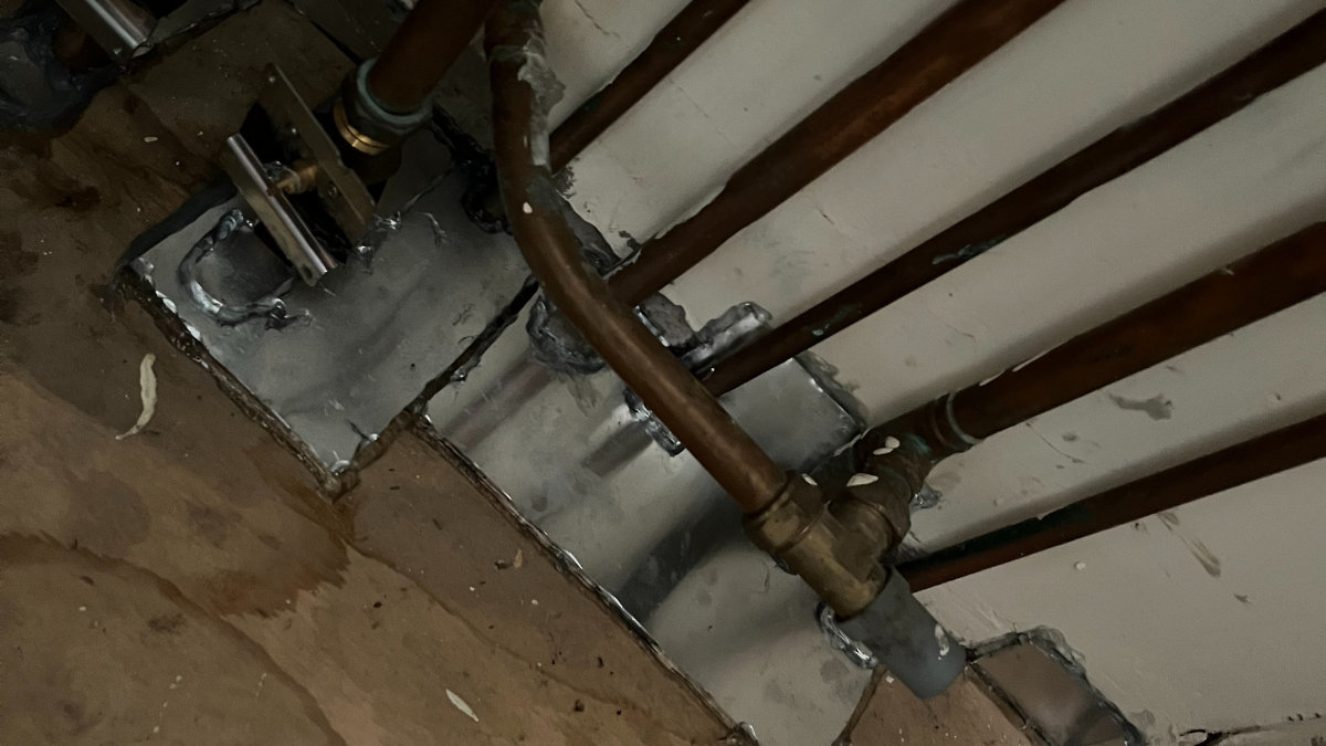Flat metal plates are attached to pipes and on a wooden floor to cover gaps.