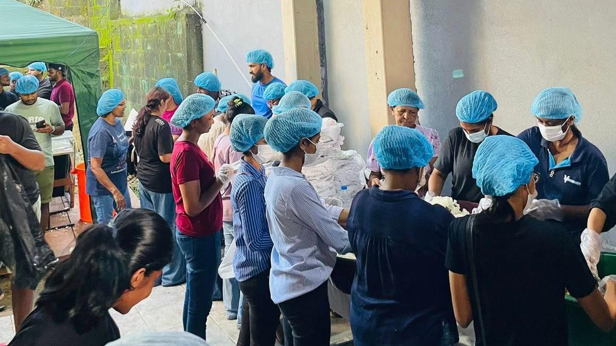Rows of people, all wearing blue hairnets, working in a makeshift kitchen