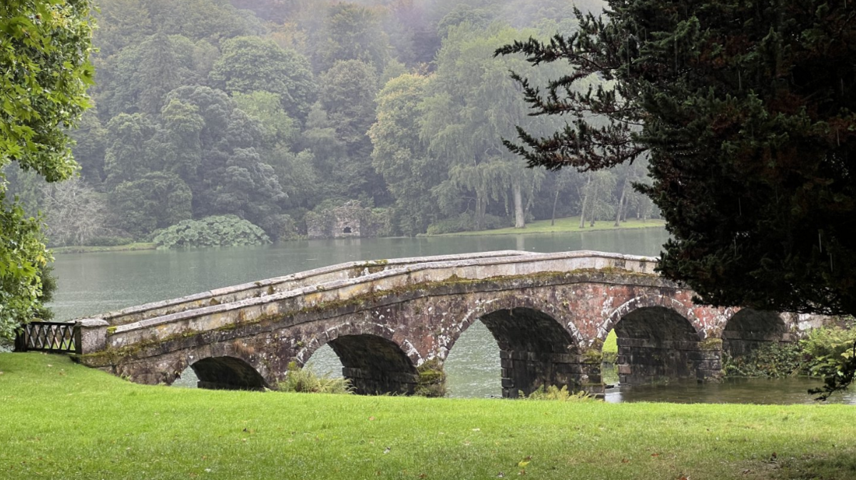 Image shows mist coming over a stone bridge within the Stourhead estate